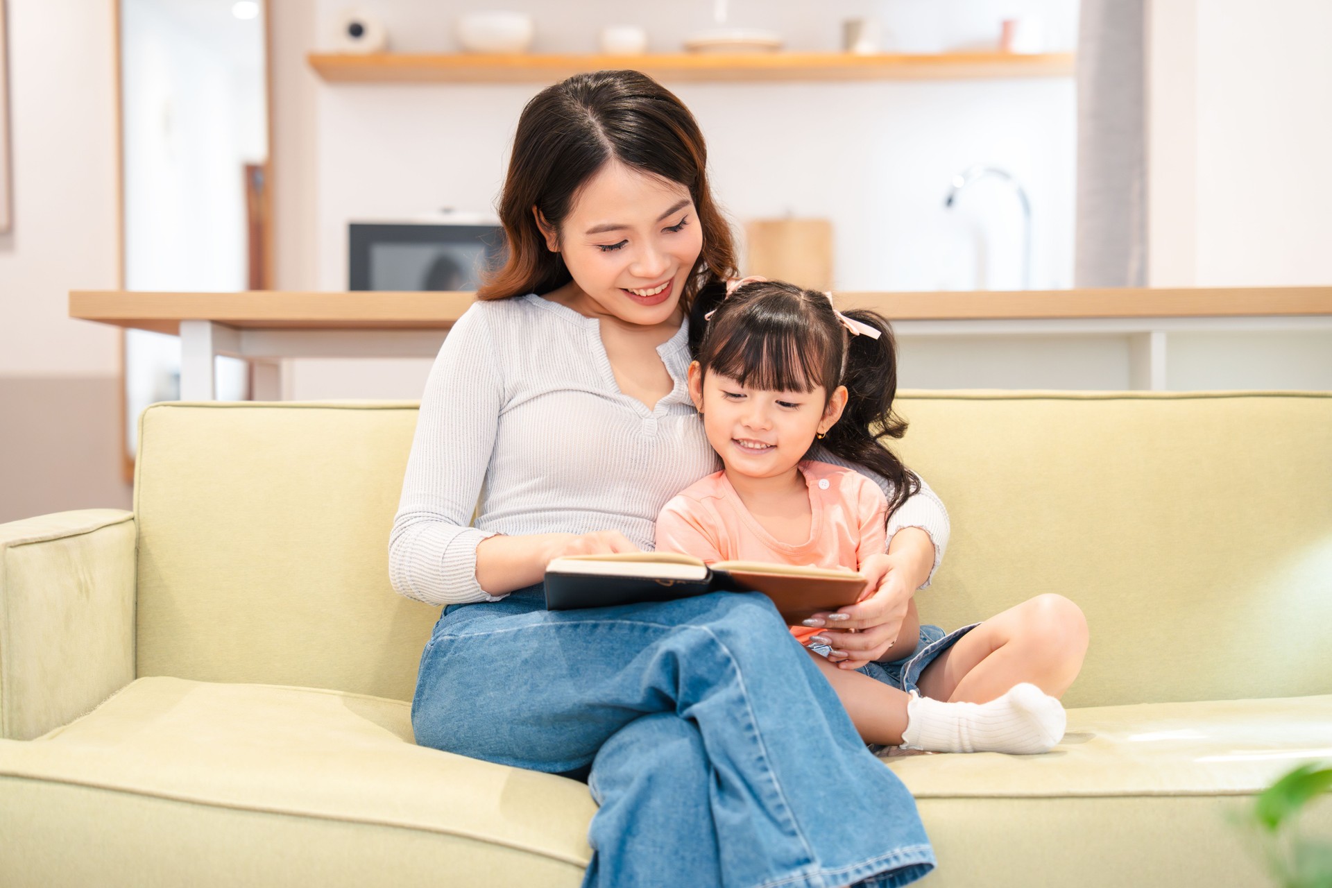 Mother and daughter share a special moment reading a story together on the cozy couch at home